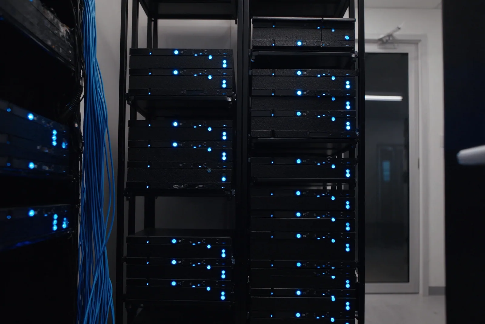 Two slim racks of plain servers with soft blue status lights in a tidy server room